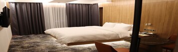 A hotel room with a large bed, a desk with a chair, and a wooden wardrobe.