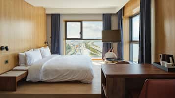 A modern hotel room with a large bed, a desk, and a view of a cityscape.