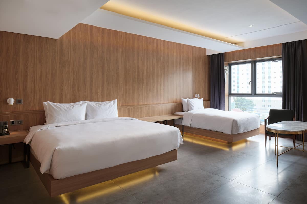 A hotel room with two beds, a desk, a chair, and a large window.