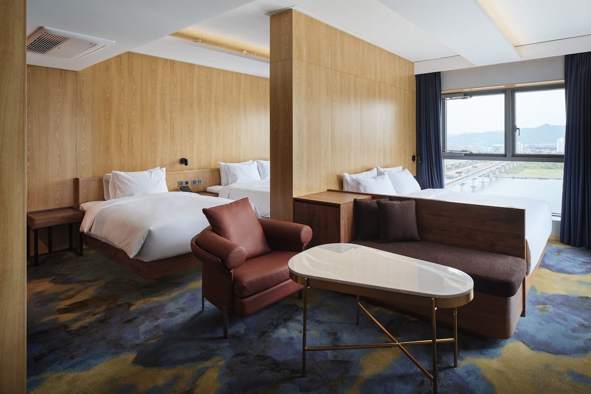 A hotel room with two beds, a sofa, a coffee table, and a view of a bridge and cityscape.