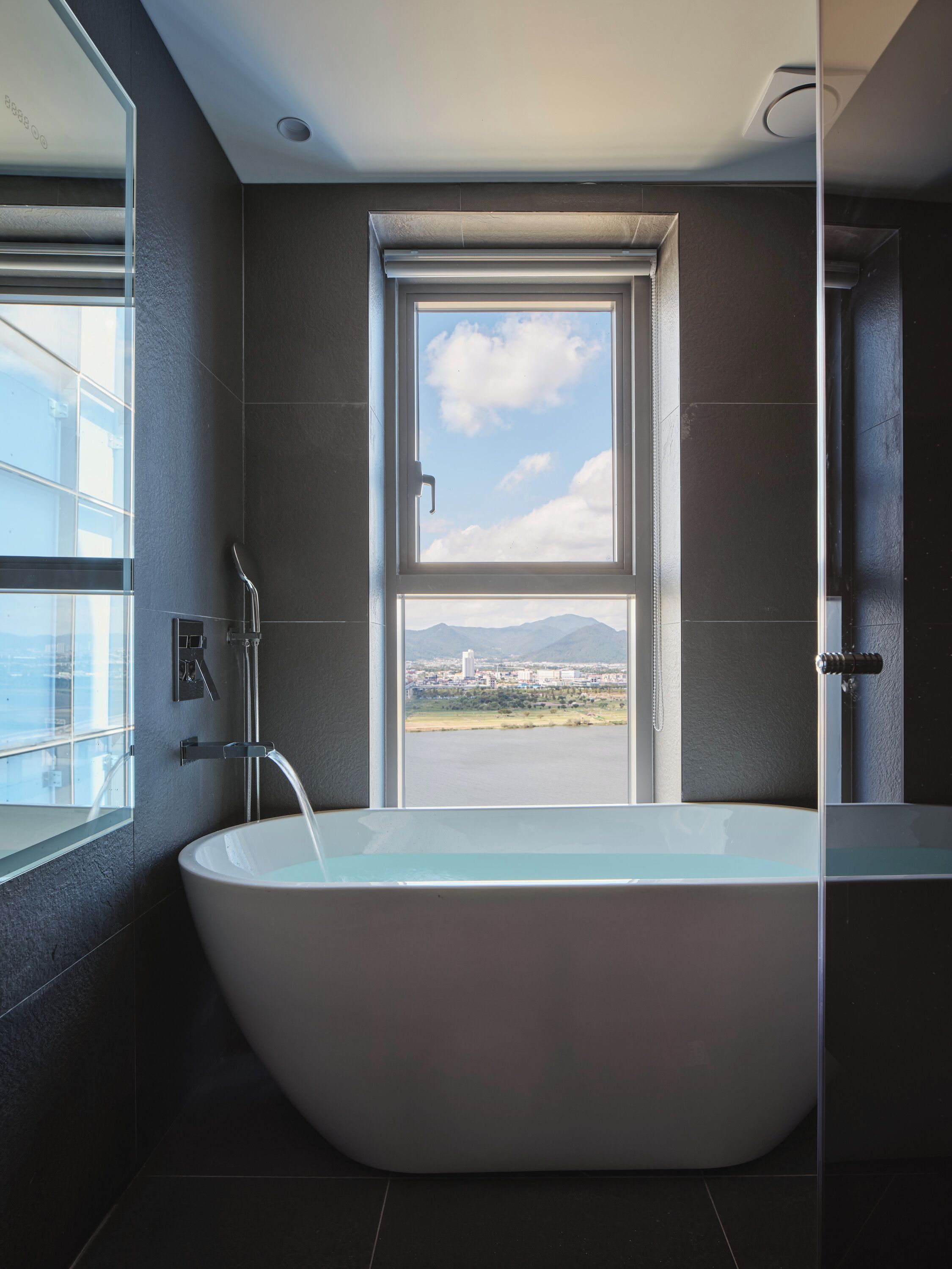 Un baño moderno con una bañera independiente, un ventanal con vistas a la ciudad y un espejo.