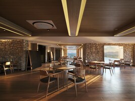 A spacious dining area with wooden tables and chairs, stone walls, and a view of the mountains.