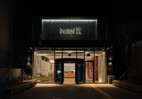 Vestíbulo de hotel con mostrador de recepción, zona de espera y una habitación de huéspedes visible.