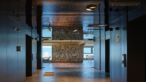 A modern elevator lobby with a stone accent wall, metal elevator doors, and a clear view of the sky through the glass. - hotel tt Gupo (Busan)