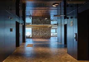 Un vestíbulo de ascensor moderno con un muro de acento de piedra, puertas de metal y una vista despejada del cielo a través del vidrio.