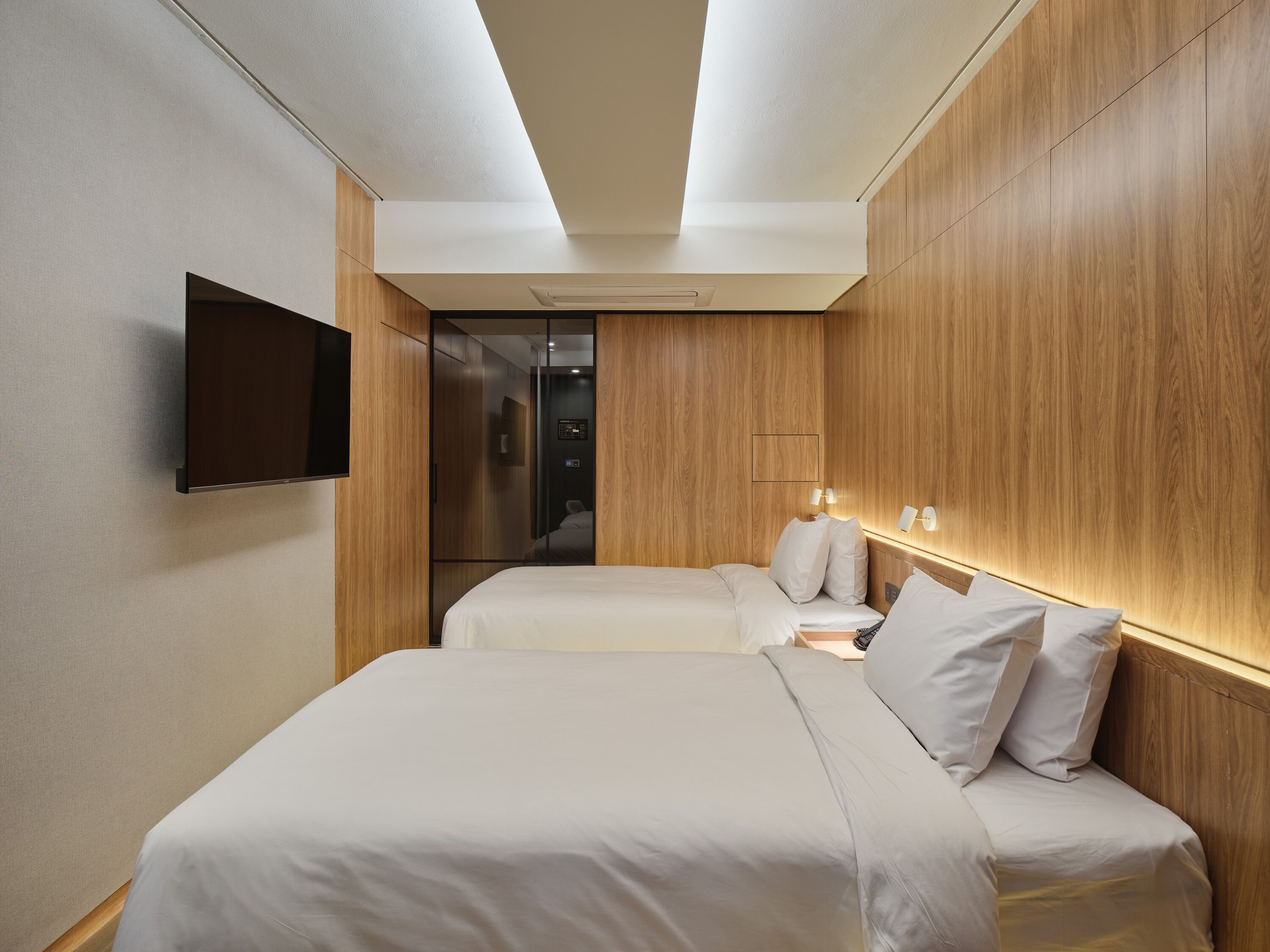 Una habitación de hotel moderna con dos camas, un televisor de pantalla plana y un panel de pared de madera.