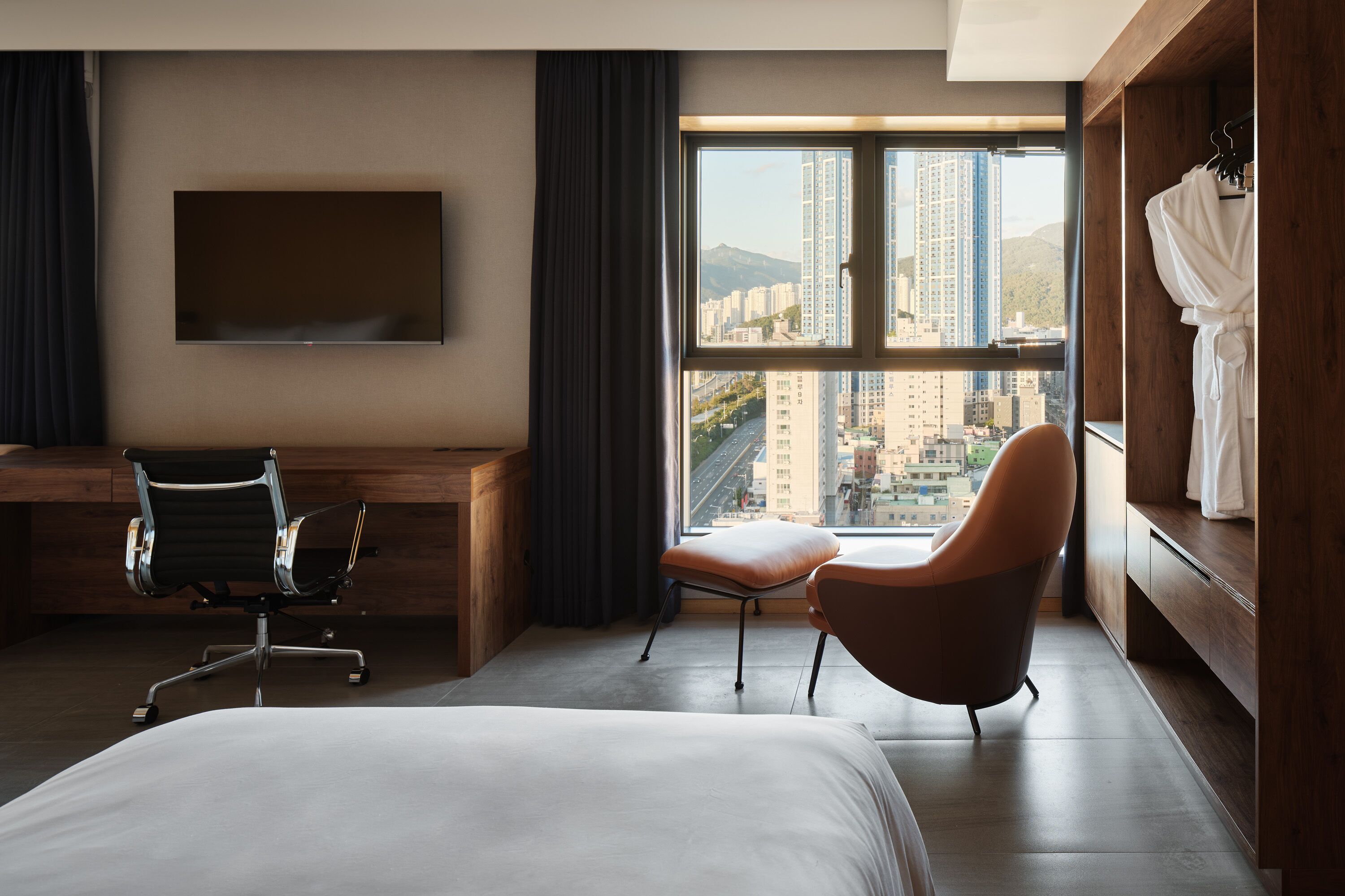 A hotel room with a bed, a desk, a chair, a TV, and a large window with a city view.
