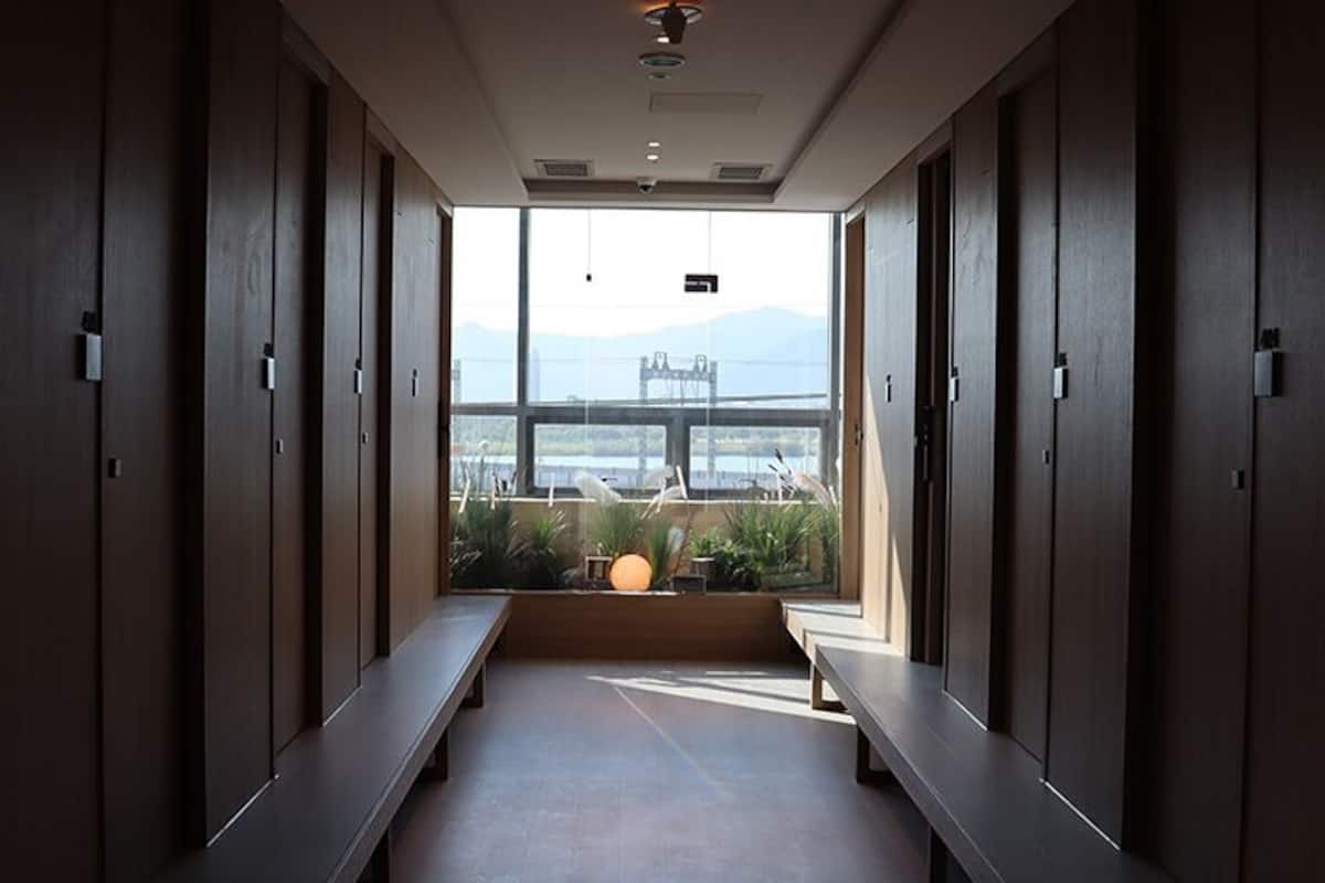 A corridor with wooden lockers and benches, leading to a large window with a view of mountains and a bridge.