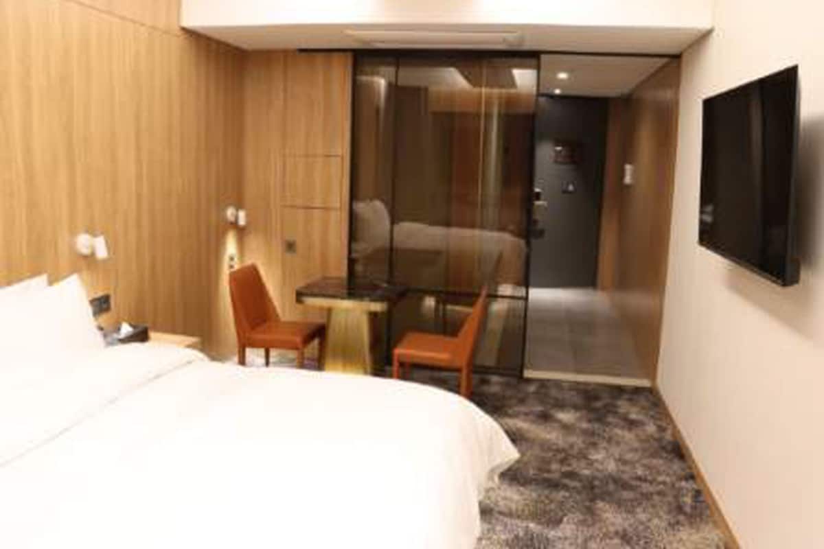 A hotel room with a bed, a desk, two chairs, a TV, and a sliding door leading to a bathroom.