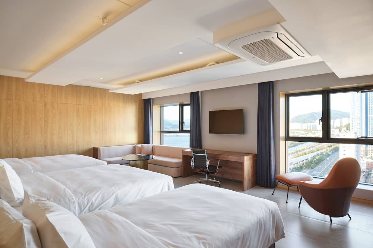 A modern hotel room with two beds, a sofa, a desk, and a TV.
