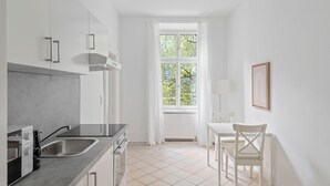 Une cuisine moderne dotée d’une grande fenêtre, de meubles blancs et d’un coin repas avec une chaise et une table.