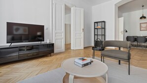 Un salon moderne avec un téléviseur à écran plat, un canapé gris, une table basse avec des livres et une bibliothèque noire.