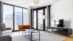 Una sala de estar moderna con un sofá, una silla, una mesa de centro, un televisor y un balcón con vistas a edificios.