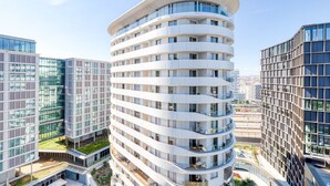 Un hotel de varios pisos con fachada curva, balcones y jardín en la azotea.