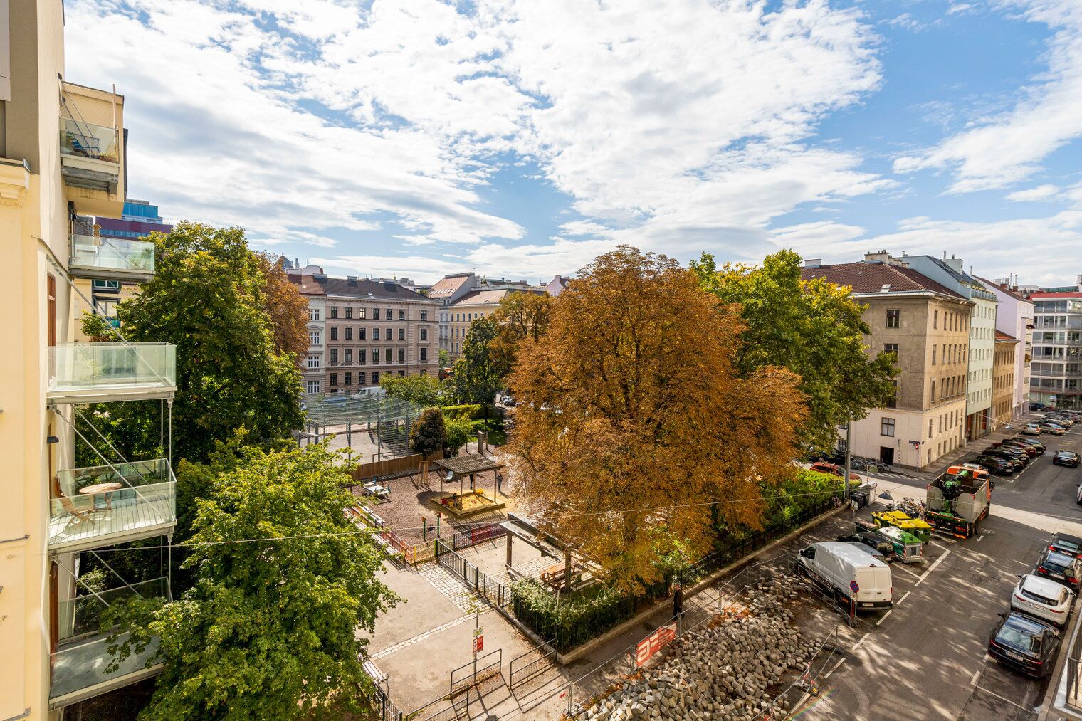 Ein mehrstöckiges Gebäude mit Balkonen, einem Innenhof mit Bäumen und geparkten Autos.