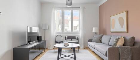 A modern living room with a sofa, a coffee table, a TV, and a window with curtains.