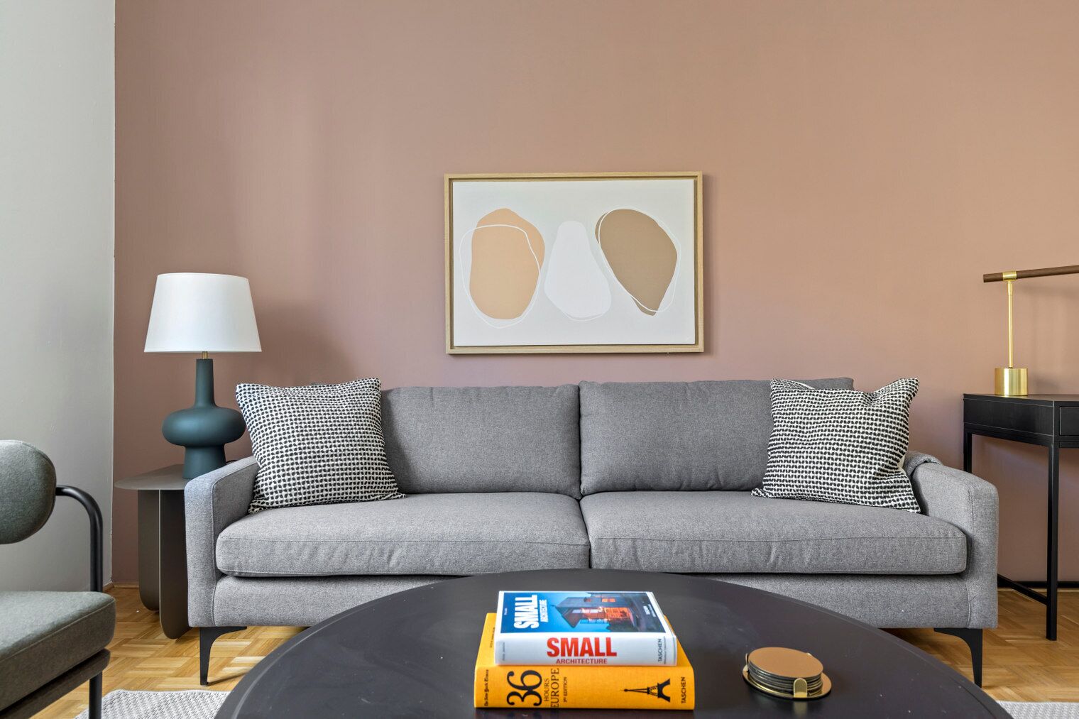 Un soggiorno moderno con un divano grigio, cuscini decorati, un tavolino da caffè nero con libri, una lampada e un'opera d'arte astratta incorniciata appesa al muro.