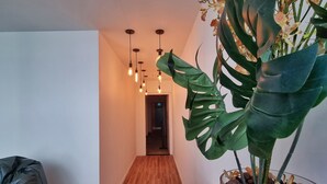 Een moderne hal met houten vloer, een kamerplant met grote bladeren en hangende lampen.