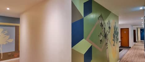 Un pasillo con un mural geométrico en la pared, suelo de madera e iluminación empotrada.