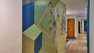 Un pasillo con un mural geométrico, suelo de madera y una puerta con el símbolo del número.