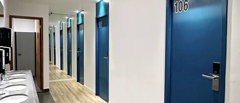 A modern hotel corridor with a long wooden floor, blue doors numbered 106 and 107, and a row of sinks on the left.