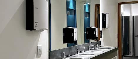 A modern bathroom with a large mirror, two sinks, and a trash bin.