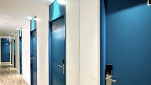 Een hotelgangen met blauwe deuren, een houten vloer en een plafond met inbouwverlichting.