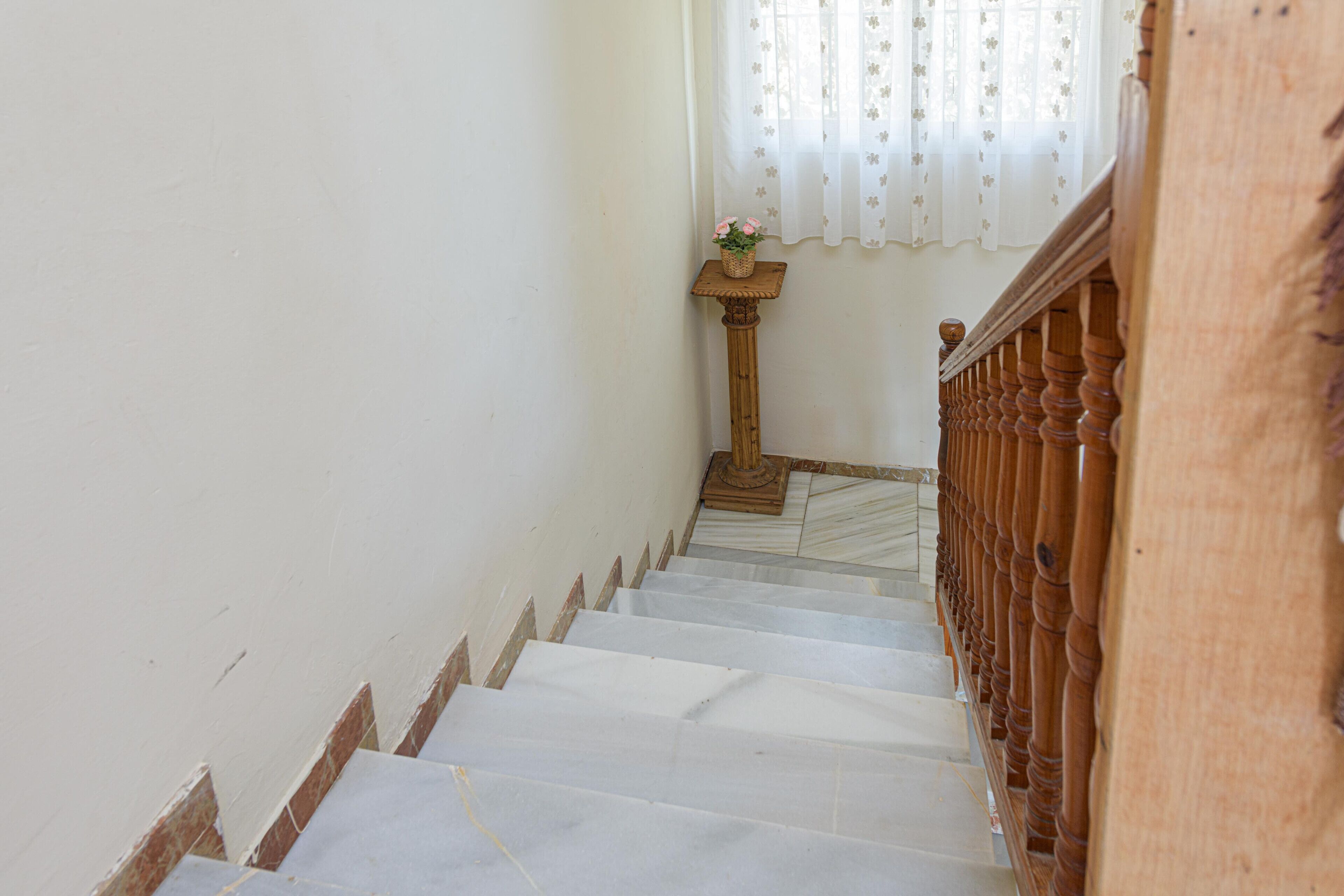Una escalera con escalones de mármol blanco, barandillas de madera y una pequeña mesa de madera con un jarrón de flores en la parte superior.