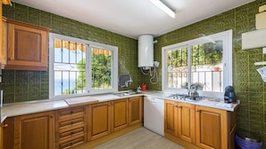 Una cocina con armarios de madera, lavavajillas, estufa y ventana con vista a follaje.