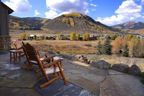 A patio with wooden chairs, a stone floor, and a view of a mountain and buildings in the distance.