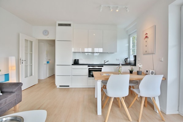 A modern kitchen with white cabinets, a dining table with chairs, and a clock on the wall.