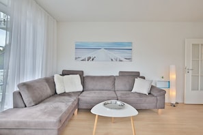 A modern living room with a grey sectional sofa, a white coffee table, and a painting of a coastal scene.