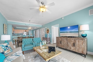 A living room with a teal sofa, a coffee table, a TV, and a cabinet. - Crystal Shores West 705 | Miles of Oceanfront Views | Indoor/Outdoor Pools | My Beach Getaways (Gulf Shores)