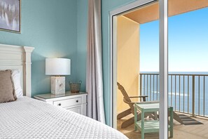 Un dormitorio con cama, mesita de noche, lámpara y vista al océano a través de una puerta corrediza de vidrio.