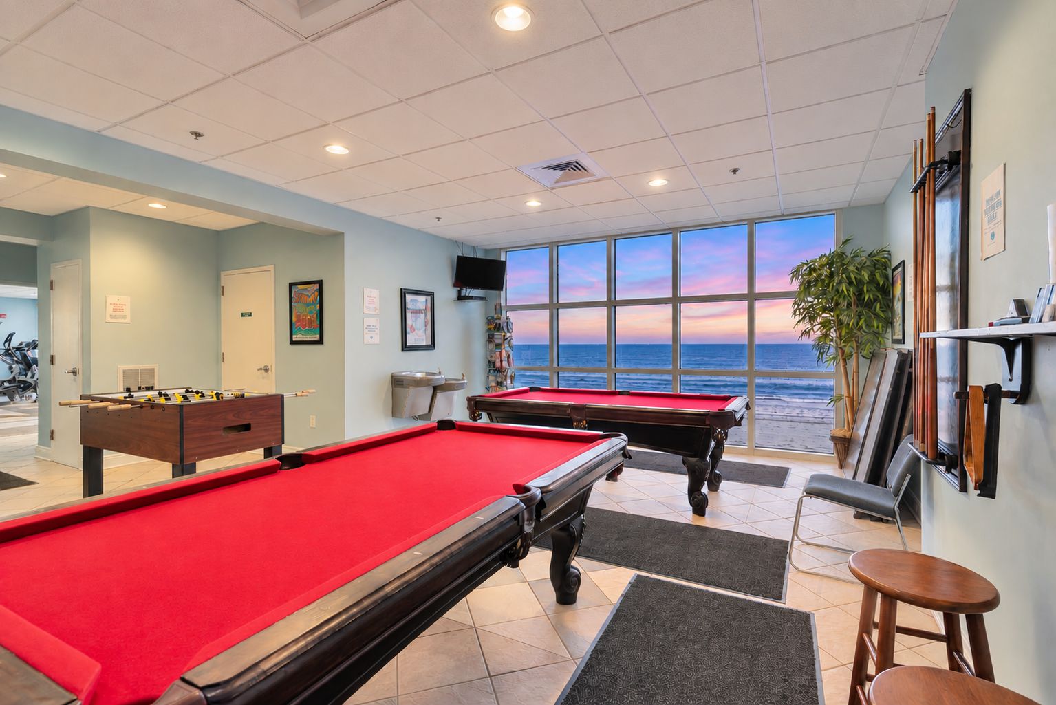 Une salle de billard avec deux tables de billard, une porte donnant sur l’extérieur et une grande fenêtre avec vue sur l’océan.