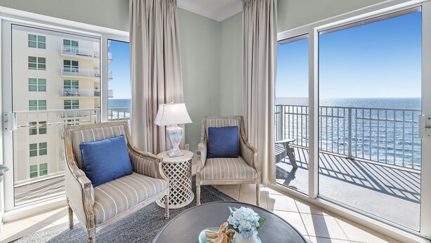 A balcony with two wicker chairs, a small round table, and a lamp. - Crystal Shores West 701 Corner Condo Wraparound Balcony | Indoor & Outdoor Pools | Beach Getaways (Gulf Shores)