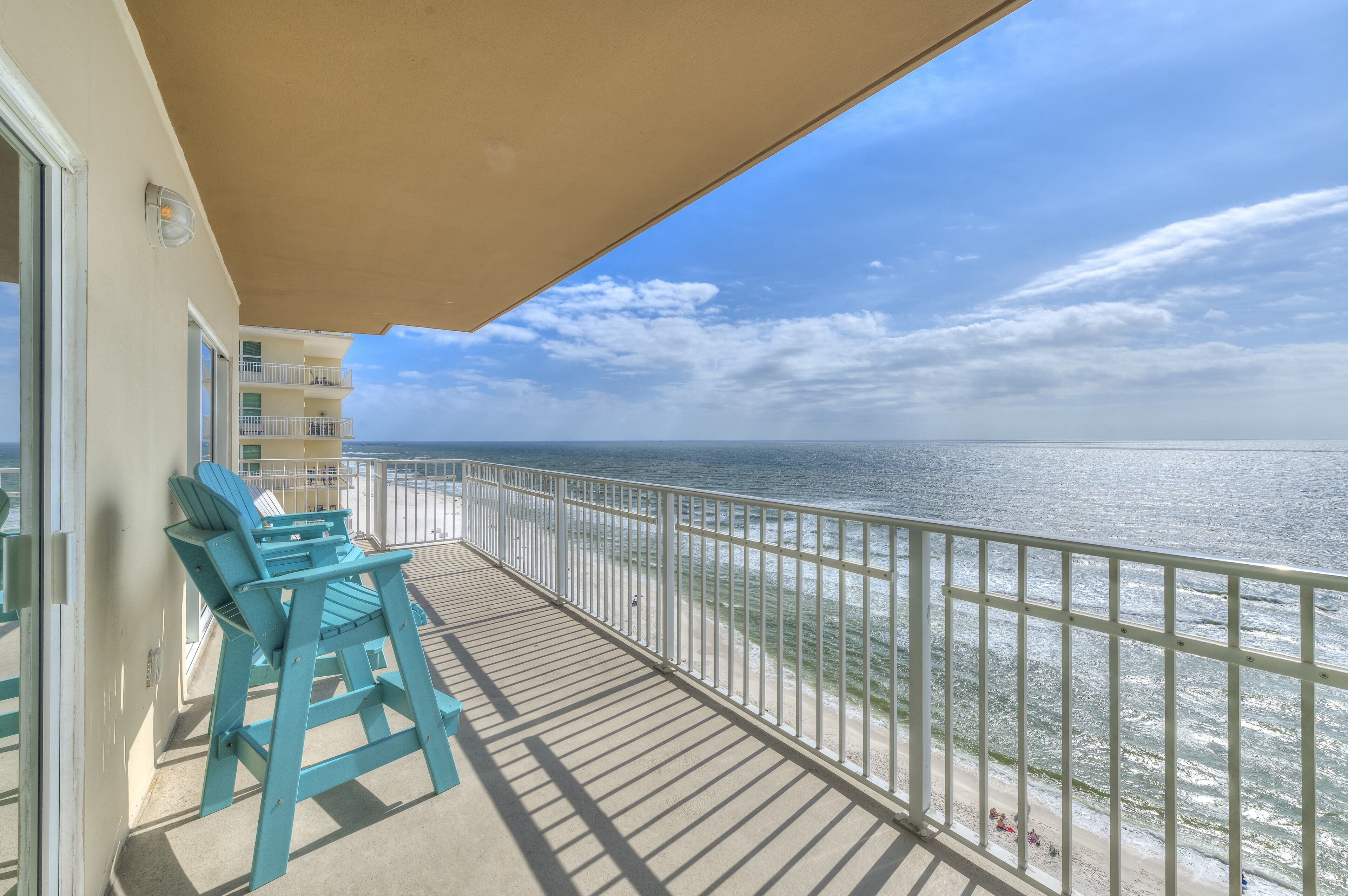 A balcony with a view of the ocean, a railing, and two blue chairs.