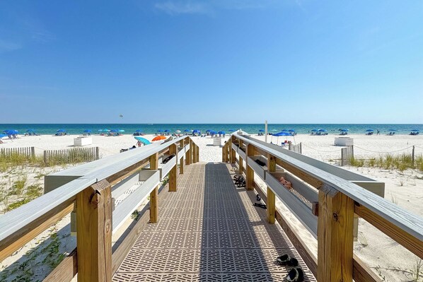 Een houten looppad naar een strand met parasols en mensen.