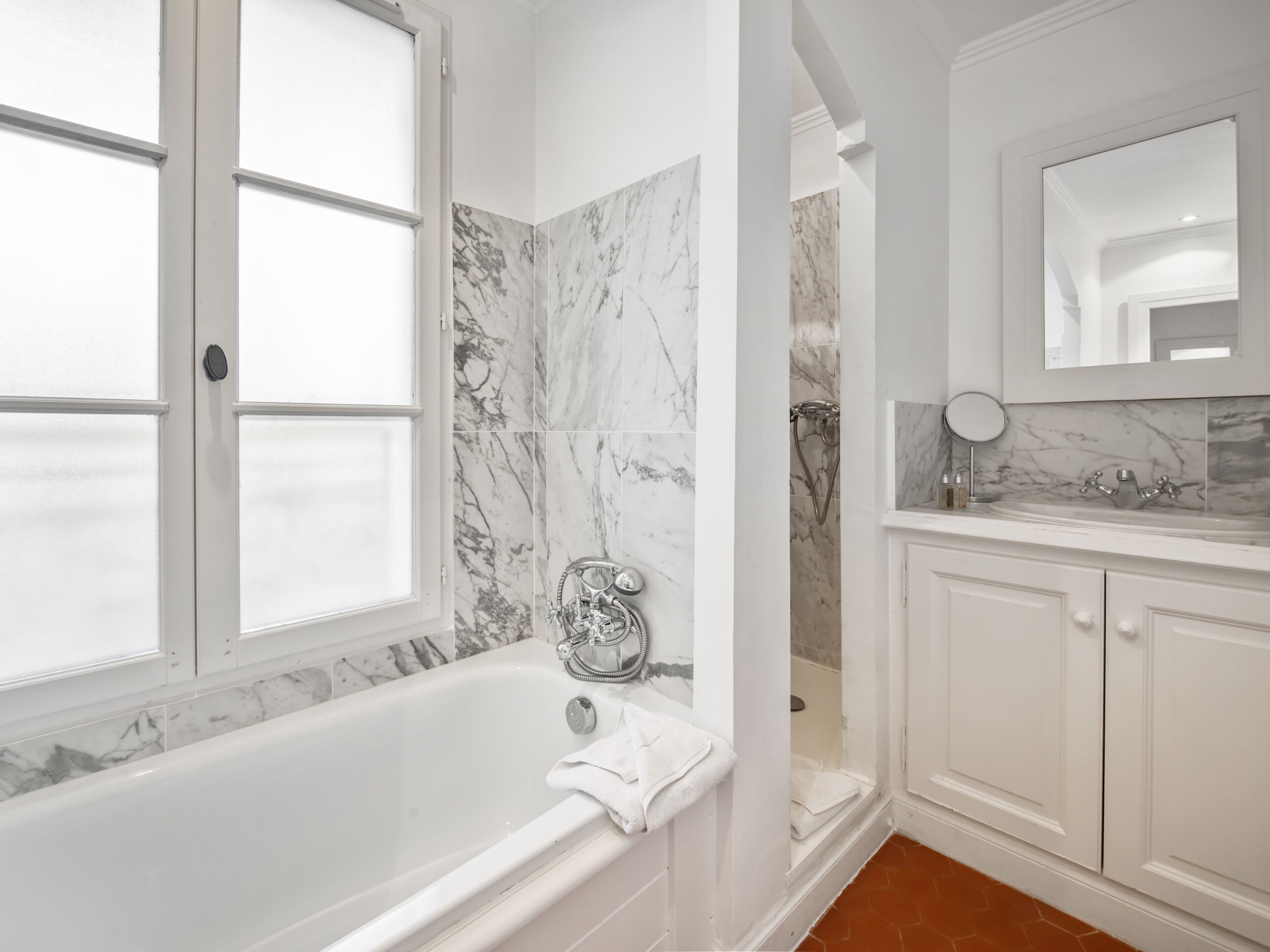 A bathroom with a bathtub, a shower, and a vanity with a mirror.