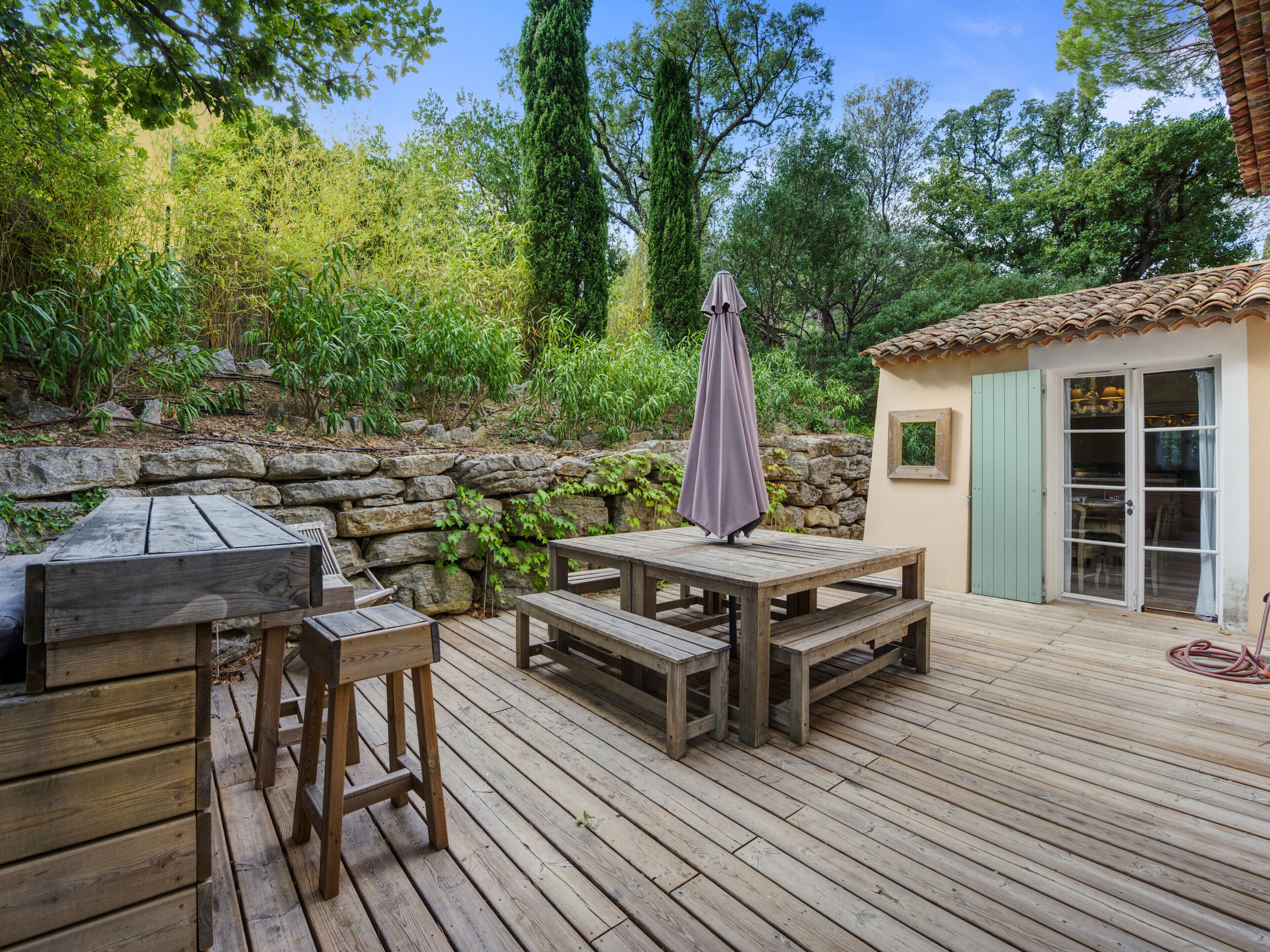 Eine Holzterrasse im Freien mit einer Steinmauer, einem Tisch und einer Bank.