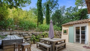 Una terraza exterior de madera con un muro de piedra, una mesa y un banco.