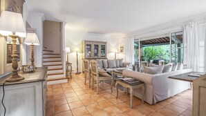 Amplia sala de estar con un conjunto de sofás, una mesa de comedor y una escalera que lleva a otro nivel.