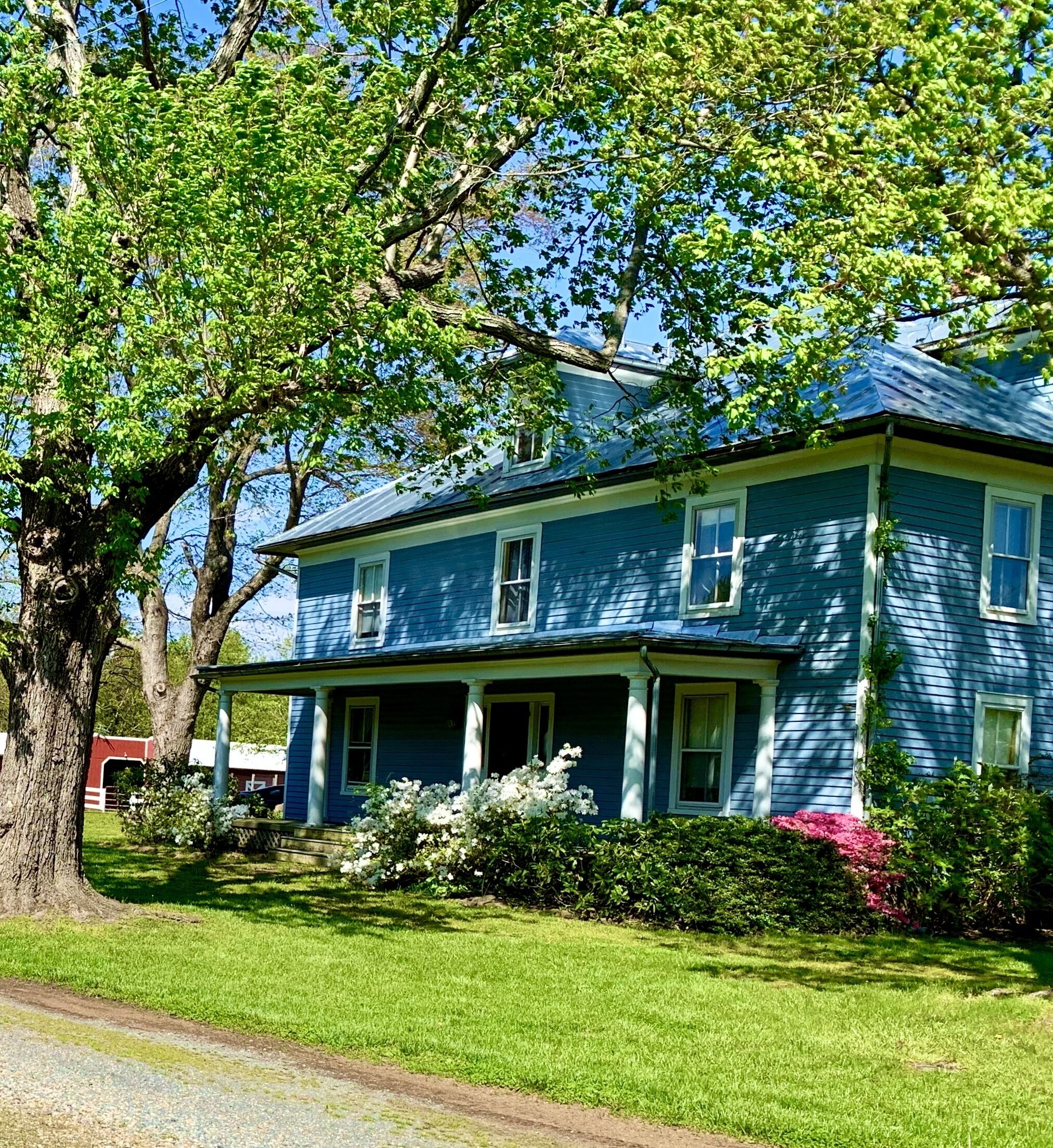A two-story house with a porch, surrounded by a well-maintained lawn and flowering bushes.
