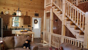 A cabin interior with a wooden staircase, a kitchen area, and a living room with a sofa and a teddy bear. - Amazing MTN Views/Location, Minutes to Gatlinburg, Hot Tub, Pool Table, WIFI (Gatlinburg)
