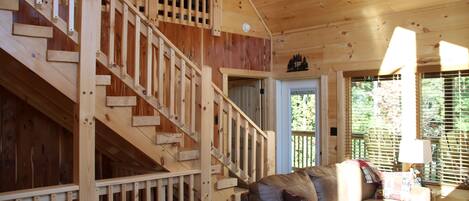 Una escalera de madera que conduce a un dormitorio en loft, una sala de estar acogedora con un sofá de cuero y una ventana con persianas.