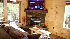 A cozy cabin interior with a stone fireplace, a flat-screen TV mounted above it, a leather couch, and a small table with decorative items. - Amazing MTN Views/Location, Minutes to Gatlinburg, Hot Tub, Pool Table, WIFI (Gatlinburg)