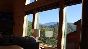 A wooden cabin interior with a large window offering a view of a forested mountain range. - Amazing MTN Views/Location, Minutes to Gatlinburg, Hot Tub, Pool Table, WIFI (Gatlinburg)