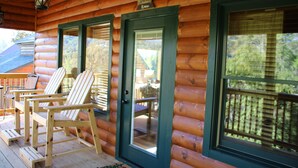 A log cabin with two Adirondack chairs on the porch, a sign above the door, and a view of the forest through the windows. - Amazing MTN Views/Location, Minutes to Gatlinburg, Hot Tub, Pool Table, WIFI (Gatlinburg)