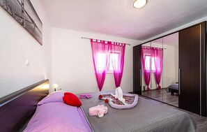 Ein Schlafzimmer mit einem Bett, einem Nachttisch, einem Spiegel und einem Fenster mit rosa Vorhängen.