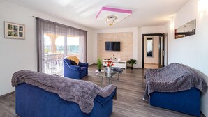 Un salon moderne comprenant un canapé, un fauteuil, une table basse et un téléviseur fixé sur un mur en pierre.